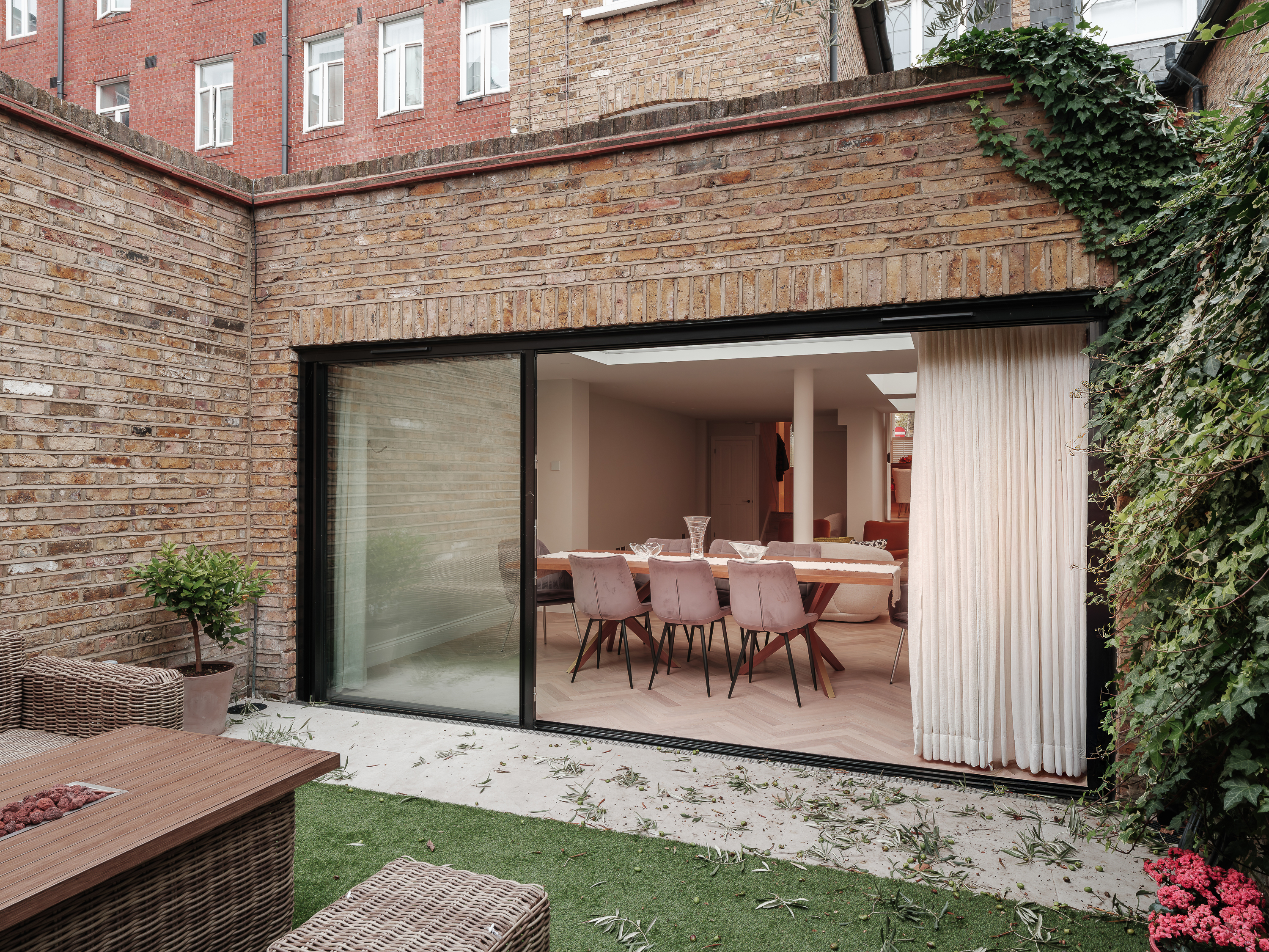Brick rear elevation with wide glazed doors opening onto a dining area